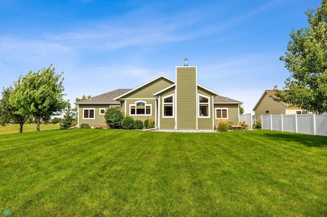 rear view of property with a yard, a chimney, and fence