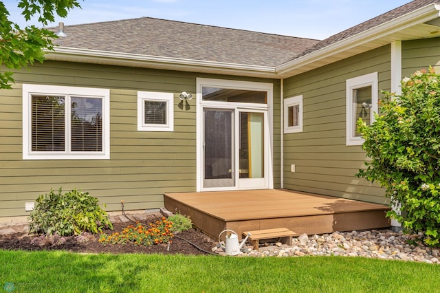 exterior space with a shingled roof, a deck, and a lawn
