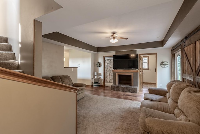 living room featuring hardwood / wood-style flooring, a fireplace, a barn door, a raised ceiling, and ceiling fan