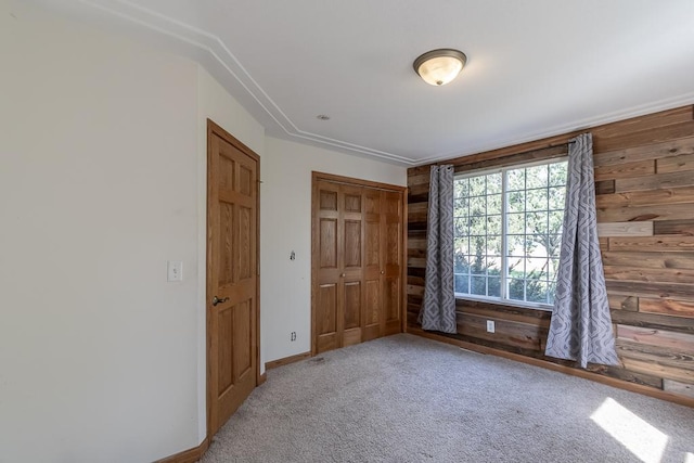 unfurnished bedroom featuring carpet flooring, wood walls, and a closet