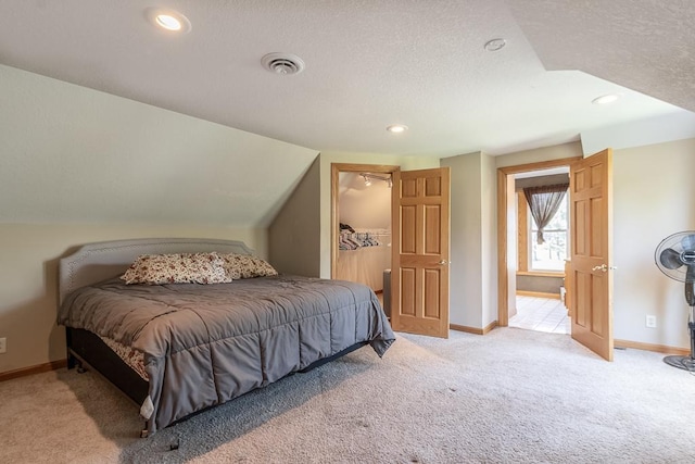 bedroom featuring a textured ceiling, light colored carpet, a walk in closet, and lofted ceiling