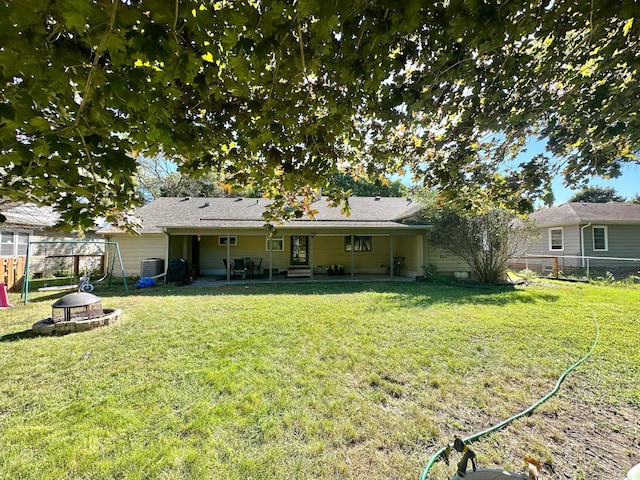 rear view of house with central AC unit, a lawn, and fence