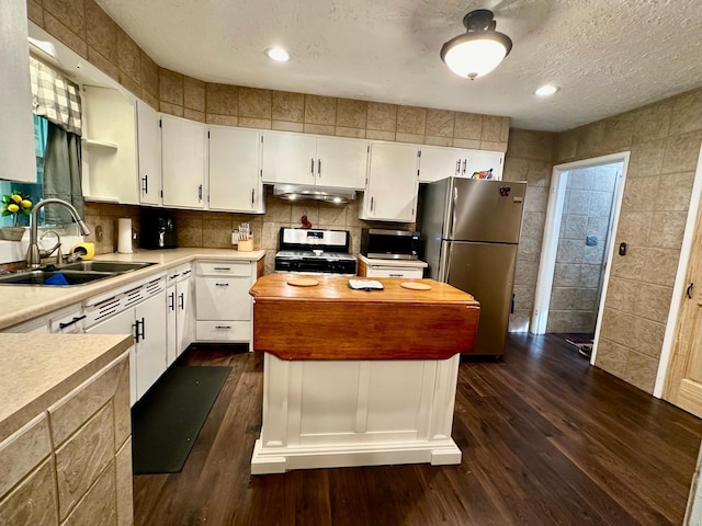 kitchen with a textured ceiling, stainless steel appliances, a sink, a center island, and dark wood finished floors