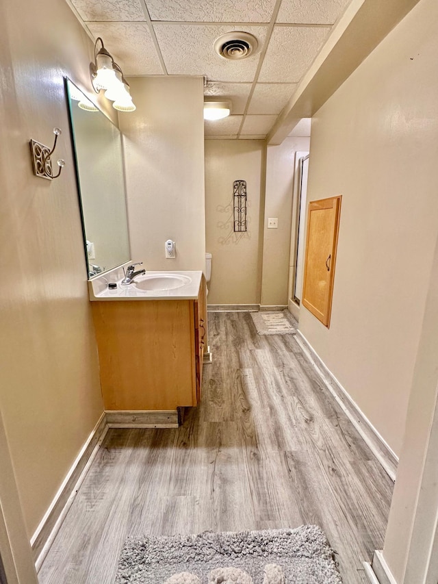 bathroom featuring a paneled ceiling, wood finished floors, vanity, visible vents, and baseboards