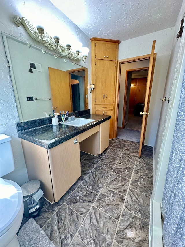 bathroom featuring visible vents, a textured ceiling, toilet, and vanity