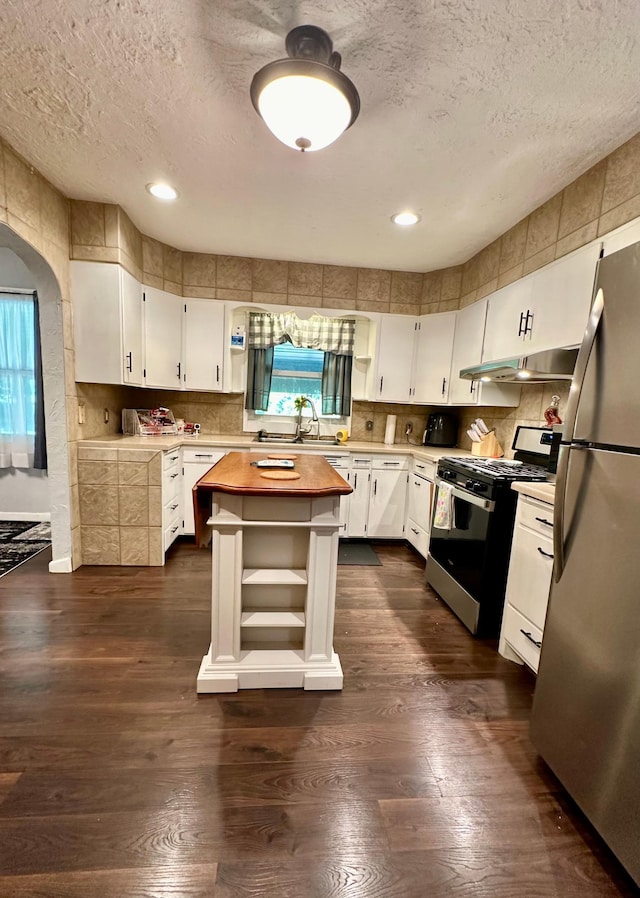 kitchen featuring white cabinets, under cabinet range hood, range with gas stovetop, and freestanding refrigerator