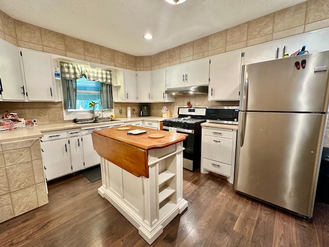 kitchen with butcher block countertops, appliances with stainless steel finishes, a sink, under cabinet range hood, and backsplash