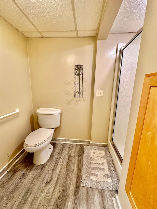 bathroom with a paneled ceiling, a shower stall, toilet, and wood finished floors