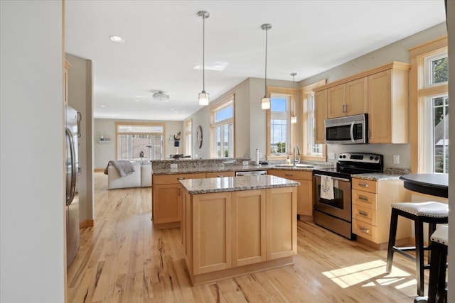 kitchen with appliances with stainless steel finishes, a healthy amount of sunlight, light hardwood / wood-style floors, and a kitchen island