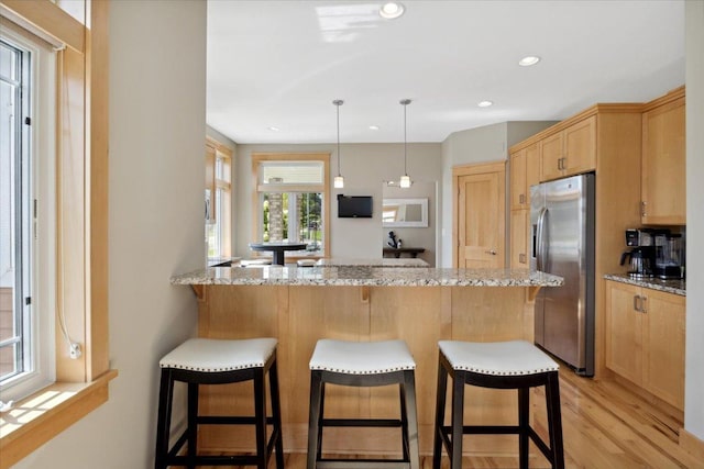 kitchen featuring light hardwood / wood-style flooring, kitchen peninsula, light stone countertops, and stainless steel fridge with ice dispenser