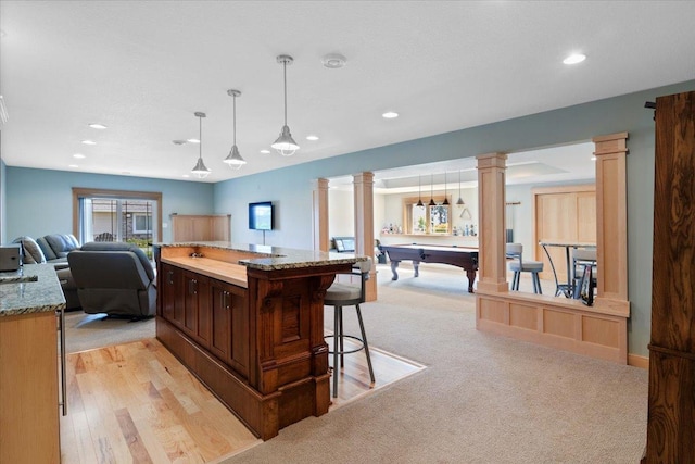 kitchen featuring light stone counters, hanging light fixtures, decorative columns, billiards, and light hardwood / wood-style floors