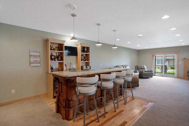 bar featuring light stone counters, light colored carpet, decorative light fixtures, and sink