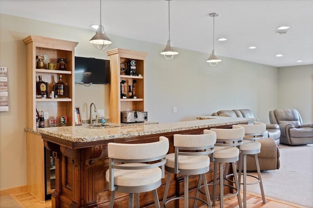 bar featuring light stone countertops, pendant lighting, sink, and light hardwood / wood-style flooring