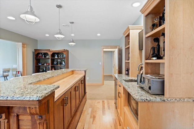 kitchen featuring light stone countertops, light wood-type flooring, decorative light fixtures, a center island with sink, and sink