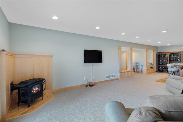 living room featuring light colored carpet, a wood stove, and ornate columns