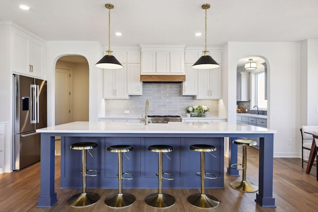 kitchen with white cabinets, decorative light fixtures, high quality fridge, and a center island with sink