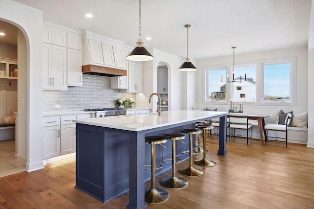 kitchen featuring decorative light fixtures, white cabinets, wood-type flooring, premium range hood, and a kitchen island with sink