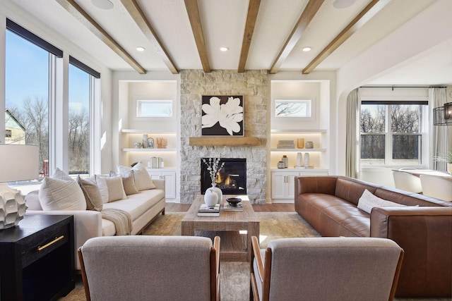 living room featuring light wood-type flooring, a stone fireplace, and beamed ceiling