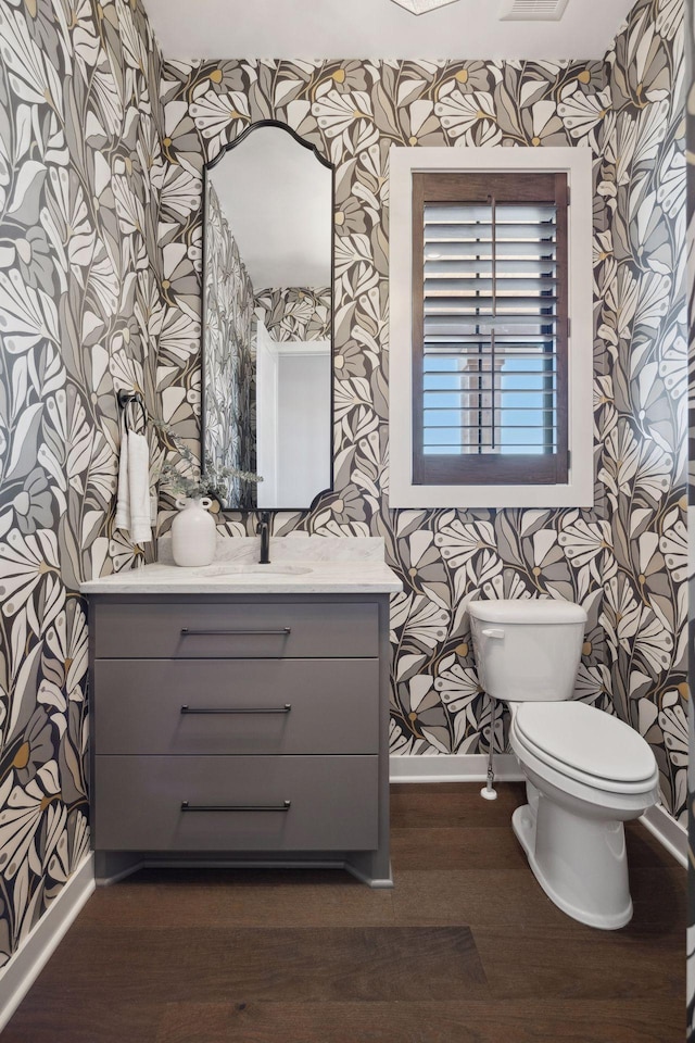 bathroom with toilet, wood finished floors, vanity, baseboards, and wallpapered walls