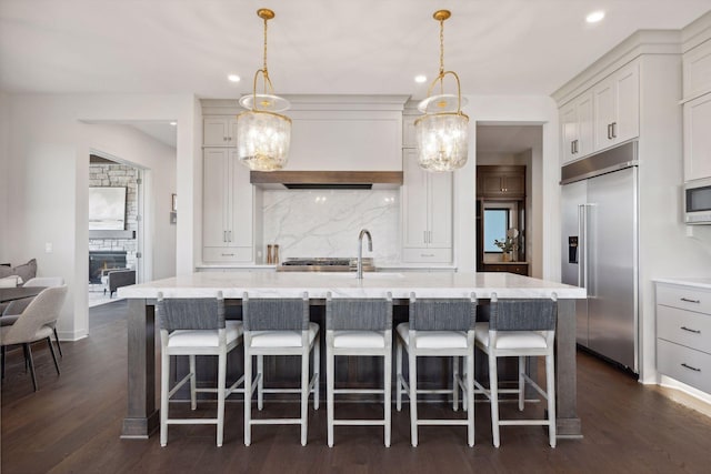 kitchen with pendant lighting, a fireplace, a center island with sink, appliances with stainless steel finishes, and a sink