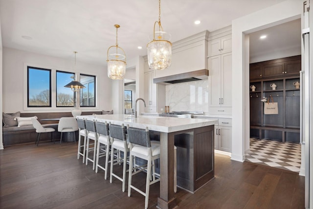 kitchen featuring a center island with sink, white cabinets, a kitchen breakfast bar, dark wood-style flooring, and decorative light fixtures