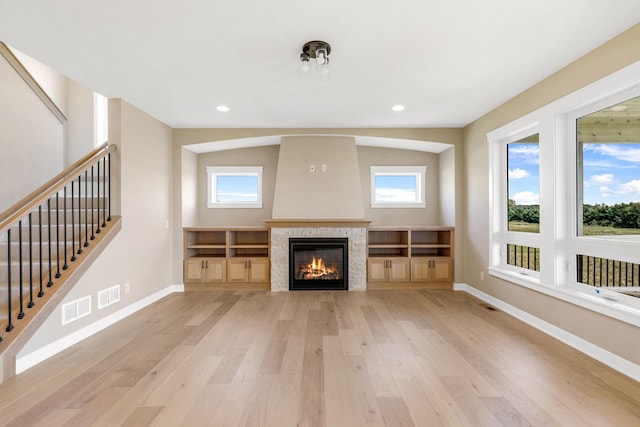 unfurnished living room featuring a tile fireplace, plenty of natural light, and light hardwood / wood-style flooring