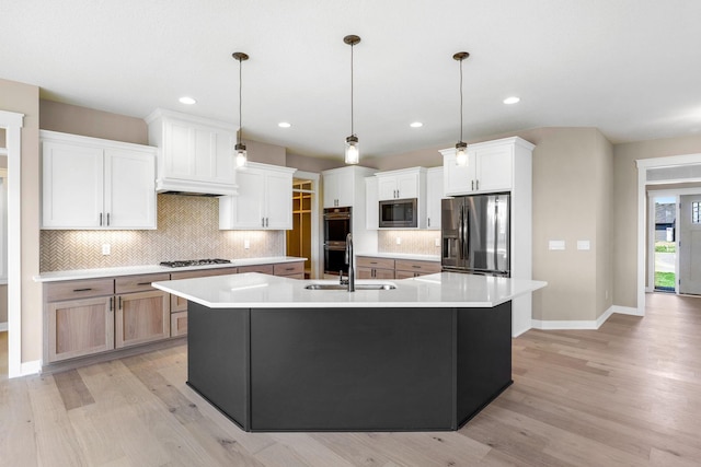 kitchen with pendant lighting, white cabinetry, light hardwood / wood-style flooring, an island with sink, and appliances with stainless steel finishes