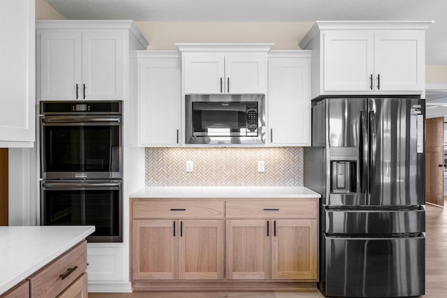 kitchen with black appliances, backsplash, white cabinets, and light hardwood / wood-style floors