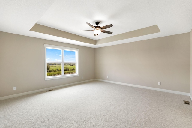 carpeted spare room with a raised ceiling and ceiling fan