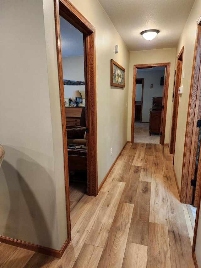 corridor with a textured ceiling and light hardwood / wood-style floors