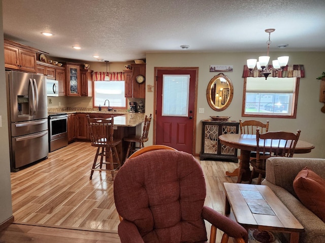 interior space featuring sink, light wood-type flooring, pendant lighting, stainless steel appliances, and light stone countertops