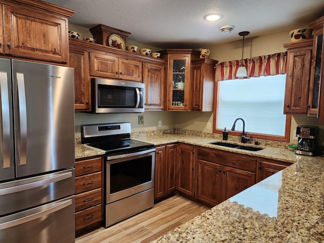 kitchen with stainless steel appliances, light stone countertops, sink, and pendant lighting