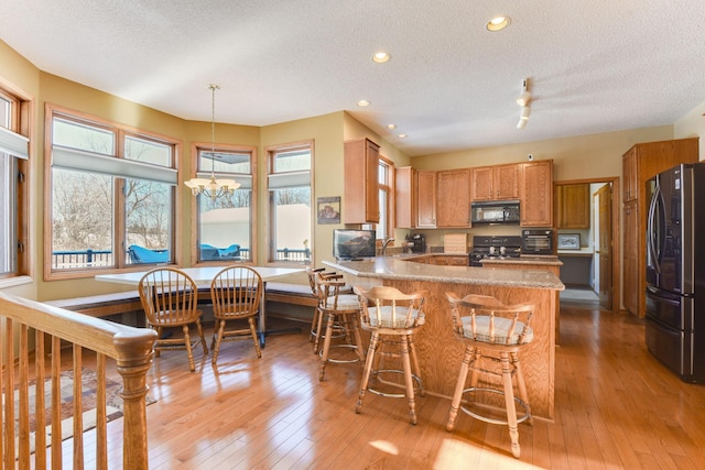 kitchen with pendant lighting, black appliances, light hardwood / wood-style floors, kitchen peninsula, and a textured ceiling