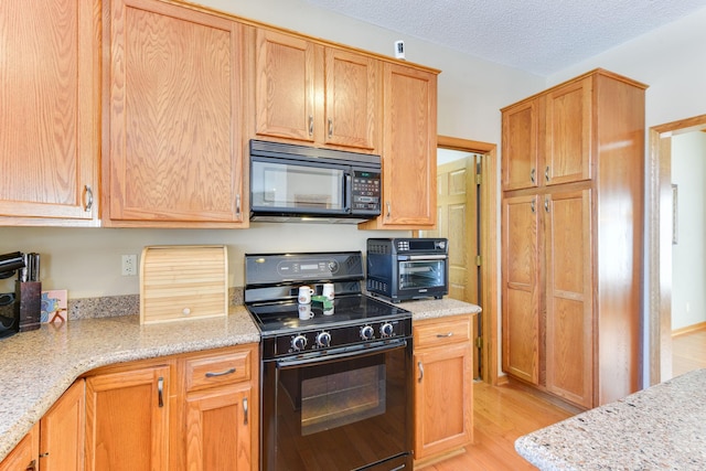 kitchen featuring light stone countertops, light hardwood / wood-style flooring, a textured ceiling, and black appliances