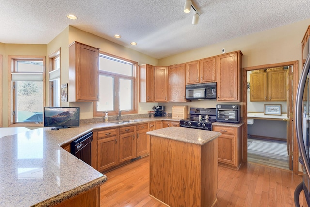 kitchen with sink, a center island, black appliances, light stone countertops, and light wood-type flooring