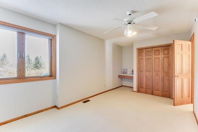 unfurnished bedroom with ceiling fan, light colored carpet, a textured ceiling, and a closet