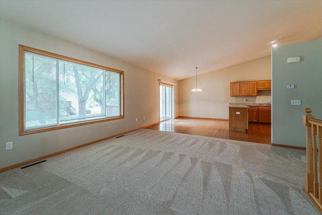 unfurnished living room featuring an inviting chandelier, light colored carpet, a textured ceiling, and vaulted ceiling