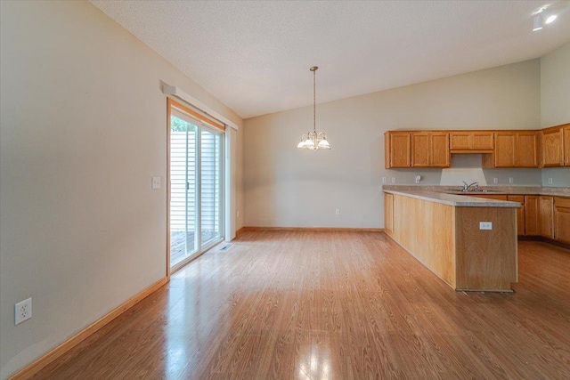 kitchen featuring kitchen peninsula, vaulted ceiling, sink, pendant lighting, and light hardwood / wood-style floors