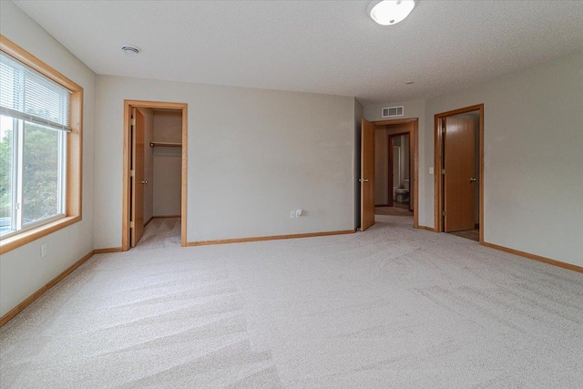 unfurnished bedroom with a textured ceiling, a walk in closet, light carpet, and a closet