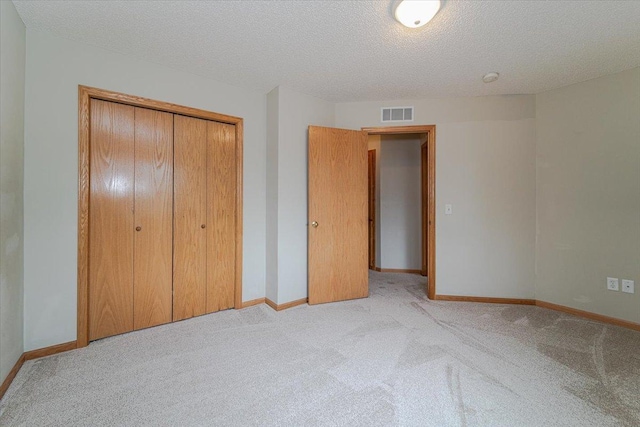 unfurnished bedroom featuring a textured ceiling, light colored carpet, and a closet