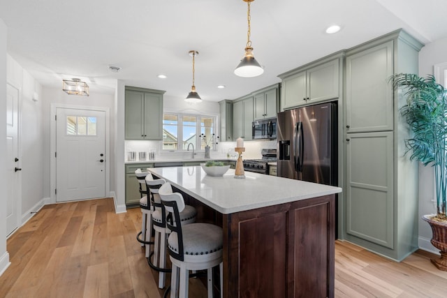 kitchen featuring light wood-type flooring, stainless steel appliances, a kitchen breakfast bar, a kitchen island, and hanging light fixtures