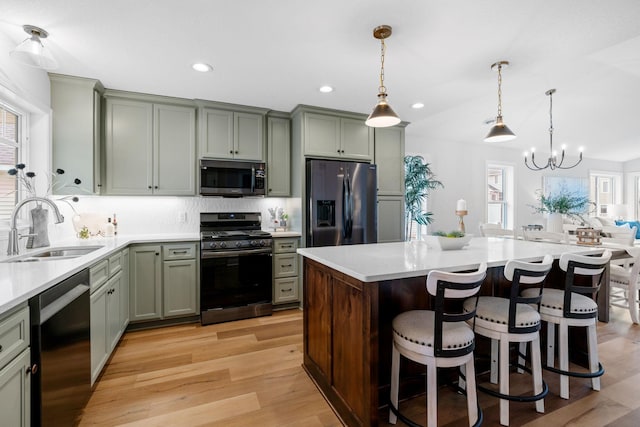 kitchen with a kitchen island, light hardwood / wood-style flooring, a notable chandelier, appliances with stainless steel finishes, and sink