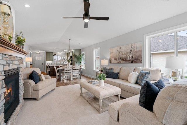 living room featuring a fireplace, vaulted ceiling, ceiling fan with notable chandelier, and light hardwood / wood-style flooring