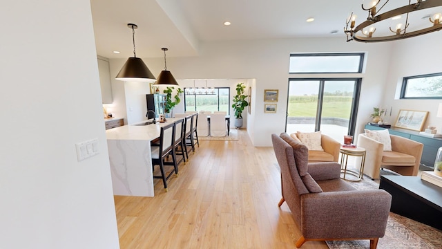 living room with a wealth of natural light, a high ceiling, light wood-type flooring, and sink