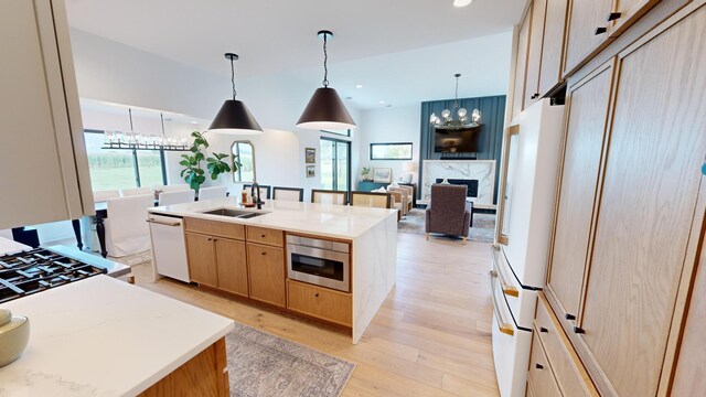 kitchen with hanging light fixtures, white appliances, a high end fireplace, light hardwood / wood-style flooring, and a kitchen island with sink