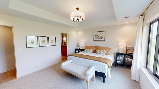 bedroom with a tray ceiling, light carpet, and a chandelier