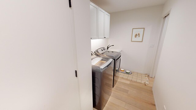 clothes washing area featuring washer and clothes dryer, cabinets, and light hardwood / wood-style floors