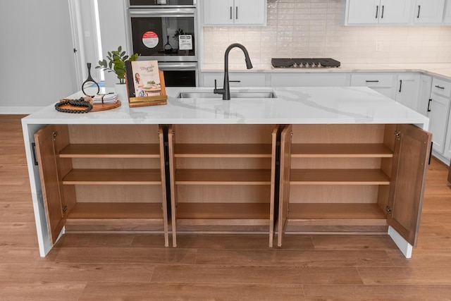 kitchen featuring open shelves, tasteful backsplash, light wood-style flooring, white cabinets, and a sink