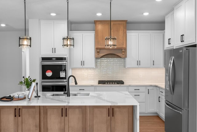 kitchen with a kitchen island with sink, appliances with stainless steel finishes, white cabinetry, and light stone counters