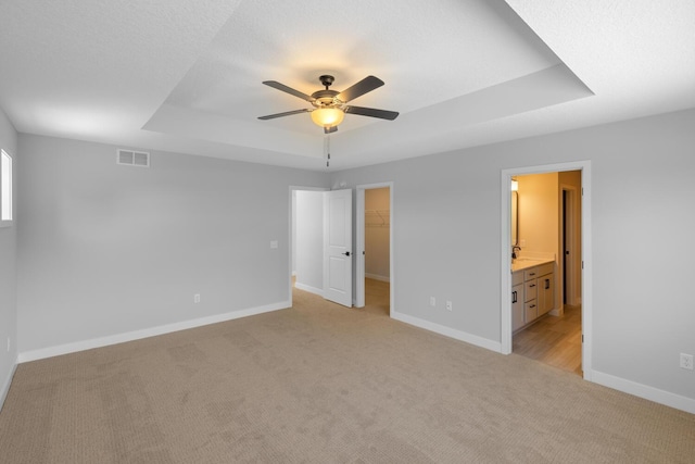 unfurnished bedroom featuring light carpet, visible vents, baseboards, a tray ceiling, and a walk in closet